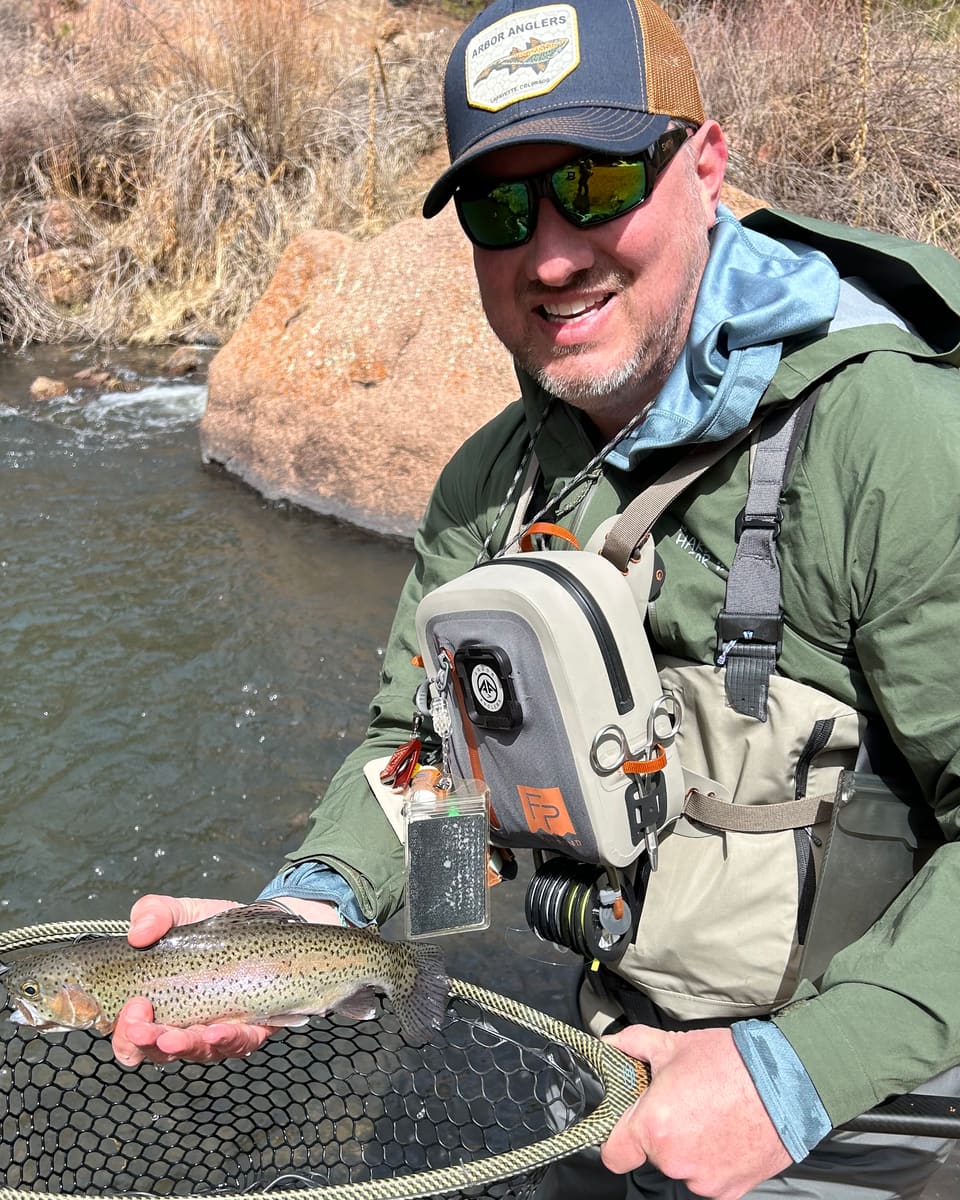 Brandon, who builds RiseCast, holding a rainbow trout in a net on a canyon tailwater.